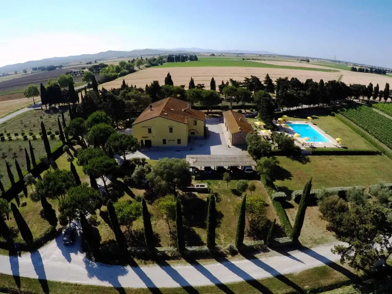 Agriturismo in Toscana con piscina, ideale per chi cerca hotel che accettano cani. Paesaggio rurale con campi dorati e cipressi.