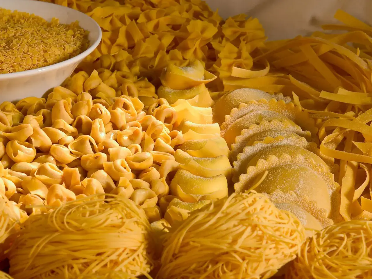 Varietà di pasta fresca, tra cui tortellini, ravioli e tagliatelle, che rappresentano i piatti tipici dell'Emilia Romagna.