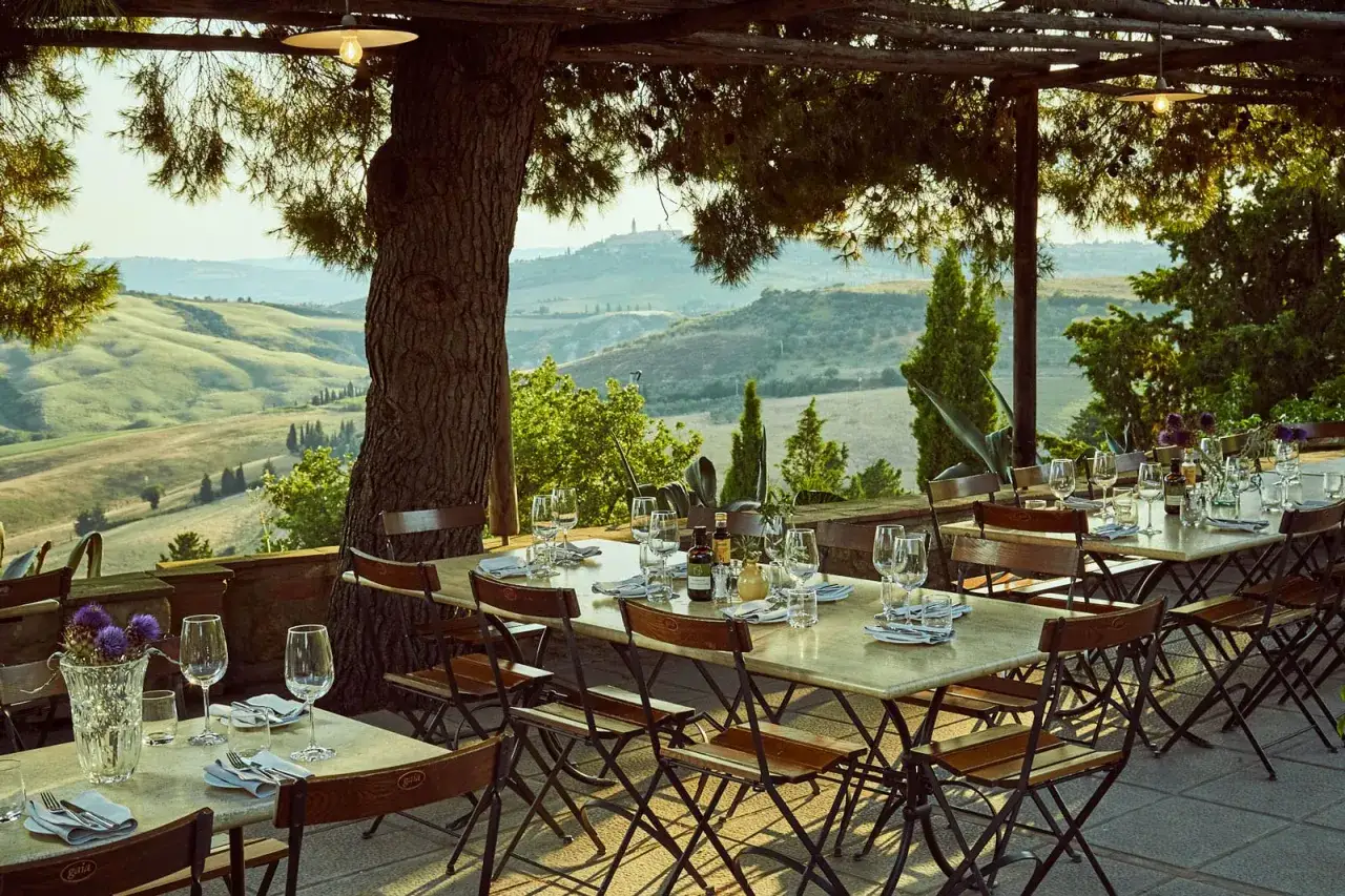Tavoli apparecchiati sotto un pergolato con vista sulle colline toscane, perfetti per visitare la Maremma e godersi un pasto all'aperto.