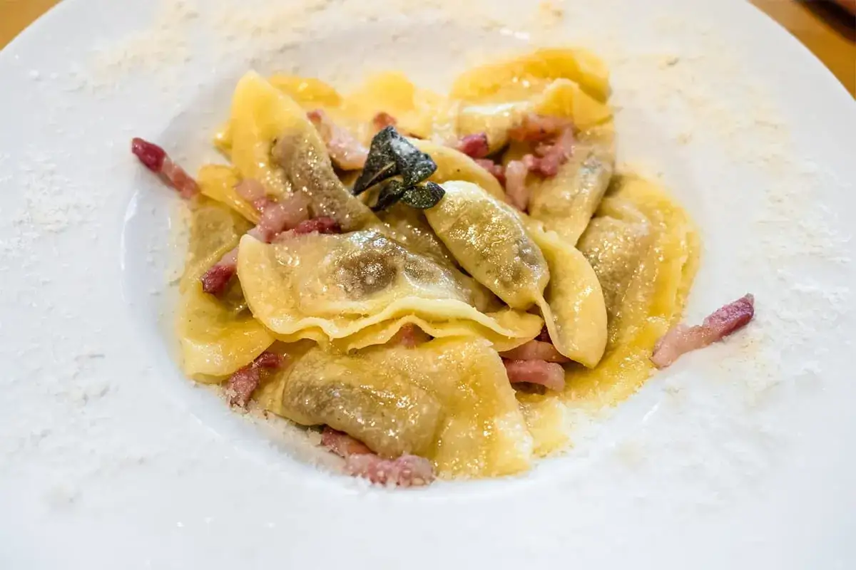 Ravioli ripieni, un piatto tipico bergamasco, conditi con pancetta croccante e una foglia di salvia.