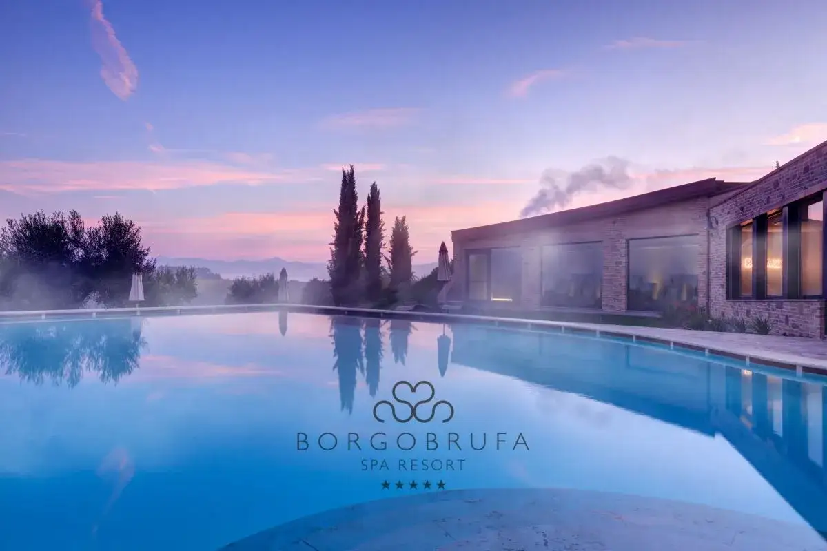 Piscina esterna di Borgobrufa Spa Resort, tra le migliori spa in Umbria, al tramonto con cielo rosa e montagne sullo sfondo.