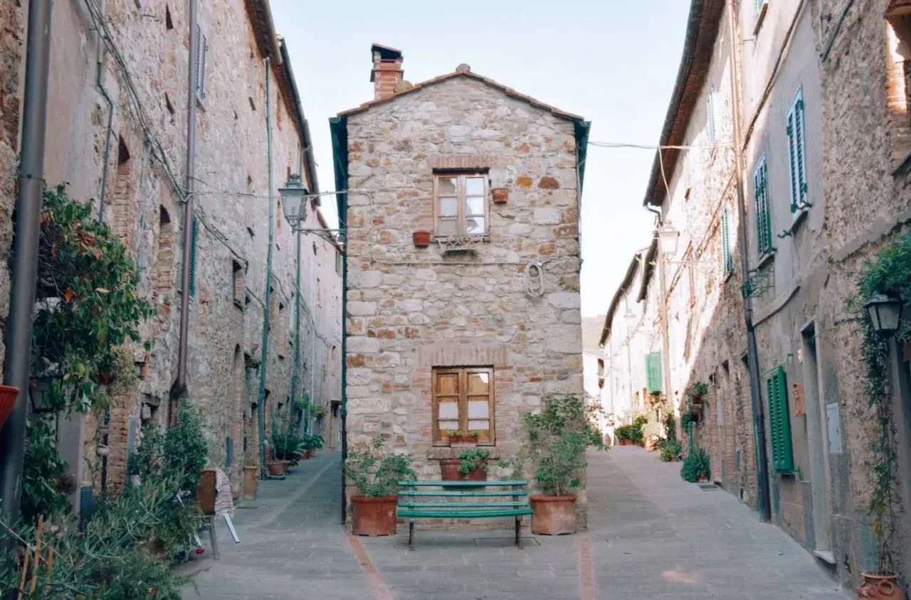 Un vicolo suggestivo, tra i borghi da visitare vicino a Cecina, con case in pietra, piante e una panchina verde.