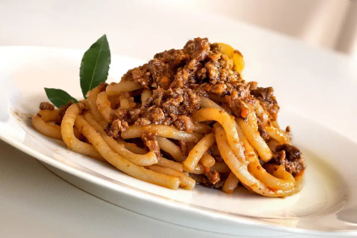 Pici fatti in casa con un ricco sugo per i pici, guarniti con foglie di alloro.