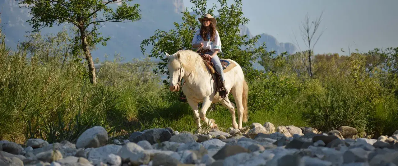Una ragazza con cappello da cowboy fa una passeggiata a cavallo in Campania, tra rocce e vegetazione rigogliosa.