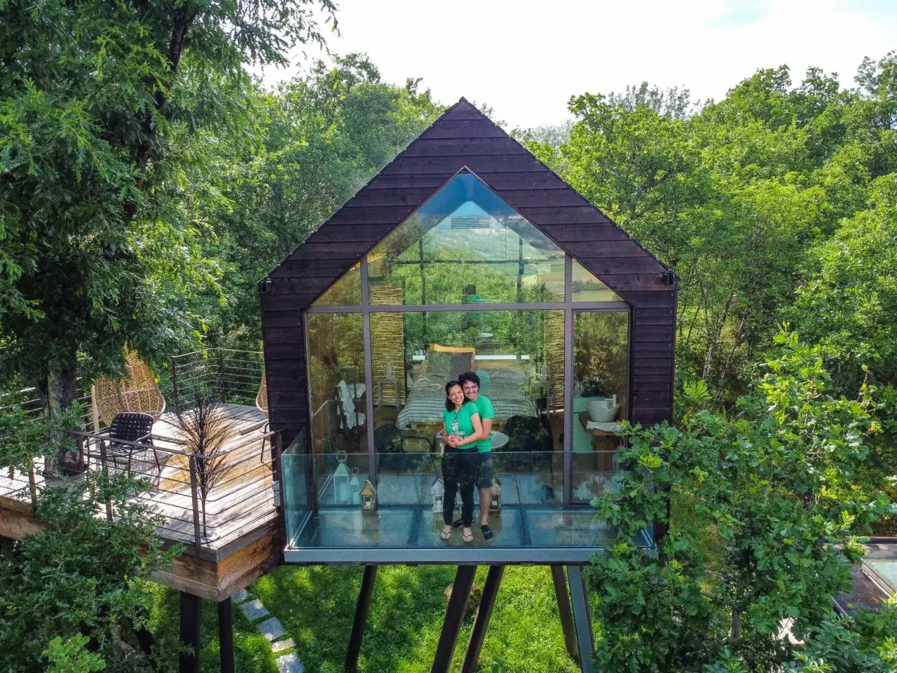 Coppia felice su una terrazza di vetro di case sull'albero, immersi nel verde.