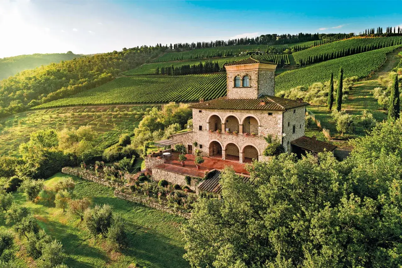 Un casale in pietra con torretta, circondato da vigneti e uliveti, incarna la bellezza delle strade del vino Toscana.