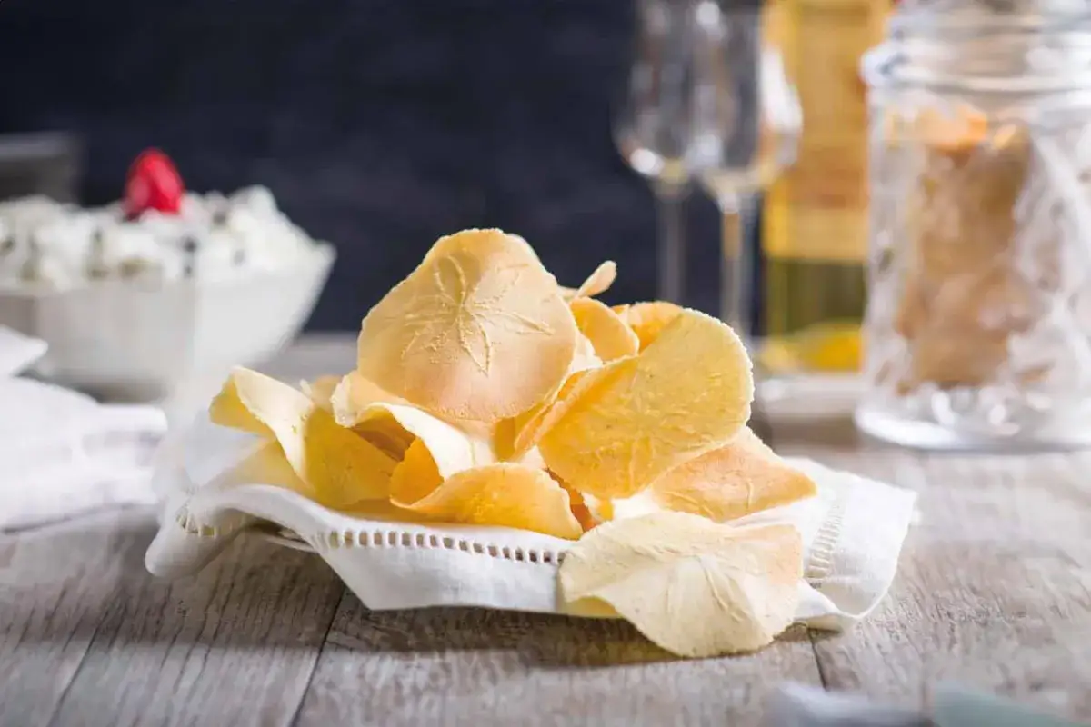 Delicati cialde, un dolce tipico toscano, servite su un tovagliolo ricamato. Sullo sfondo, una ciotola con crema e bicchieri.