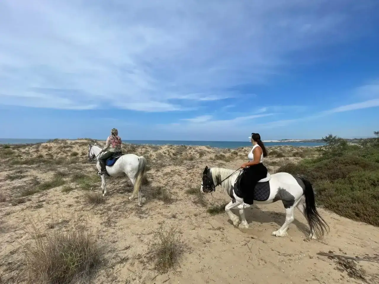 Due donne fanno una passeggiata a cavallo in Sicilia, su un sentiero sabbioso vicino al mare.