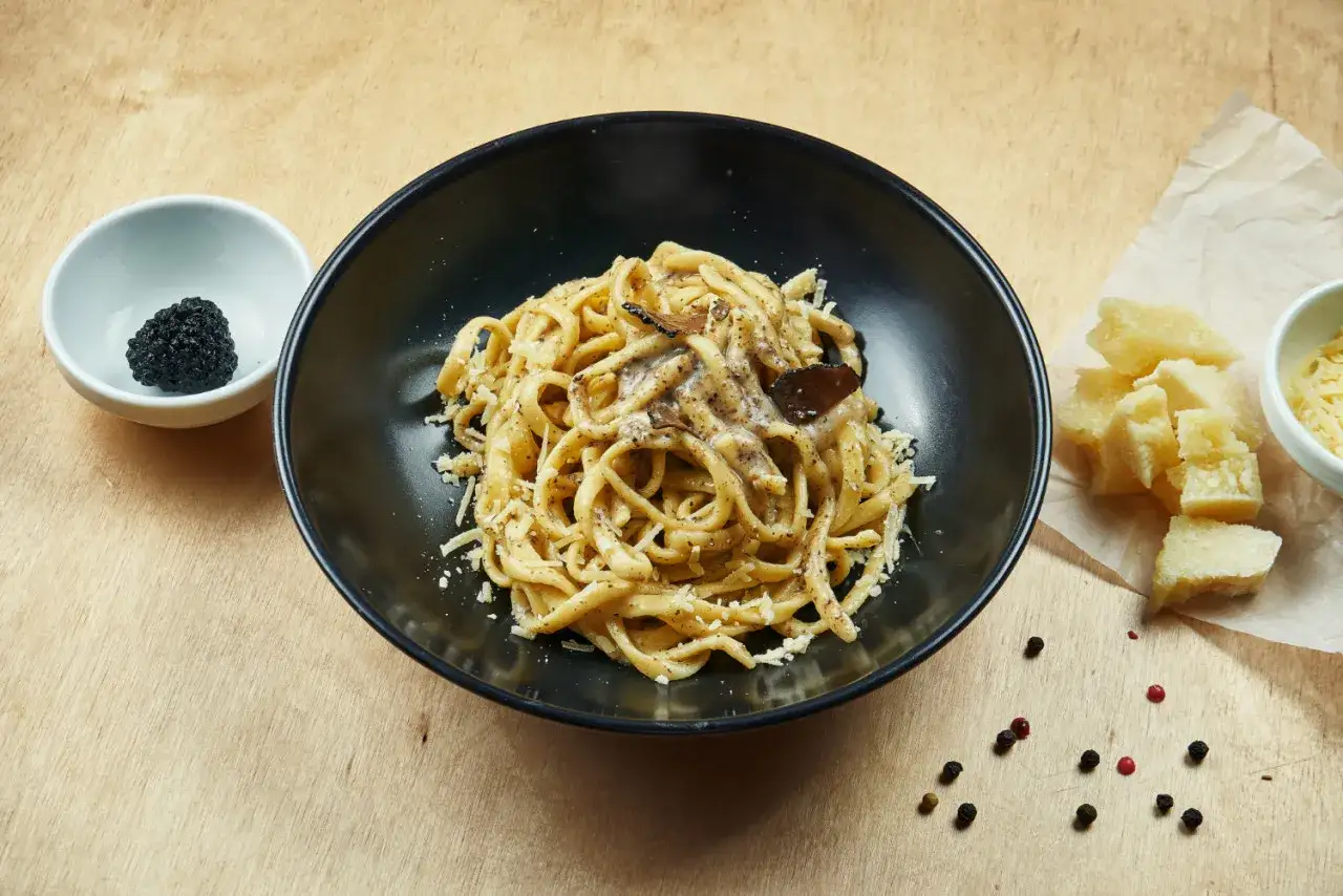Un piatto di pasta al tartufo, un'eccellenza del cibo a Perugia, con scaglie di parmigiano e pepe nero.