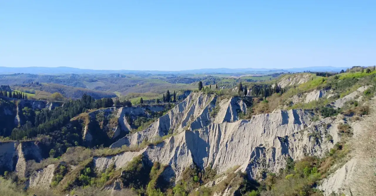 Paesaggio lunare con calanchi toscana, creste erose e vegetazione verdeggiante sotto un cielo azzurro.