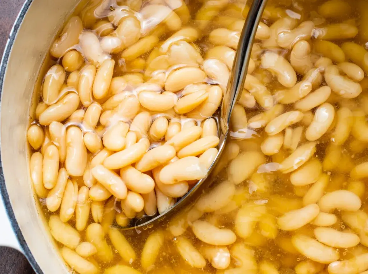 Un mestolo raccoglie fagioli borlotti in un tegame, un classico delle ricette della cucina povera toscana.