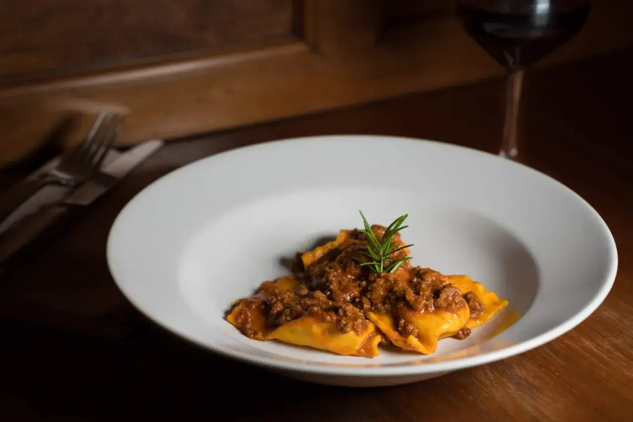 Tortelli di patate del Mugello, un piatto ricco e saporito, servito su un piatto bianco con un rametto di rosmarino.