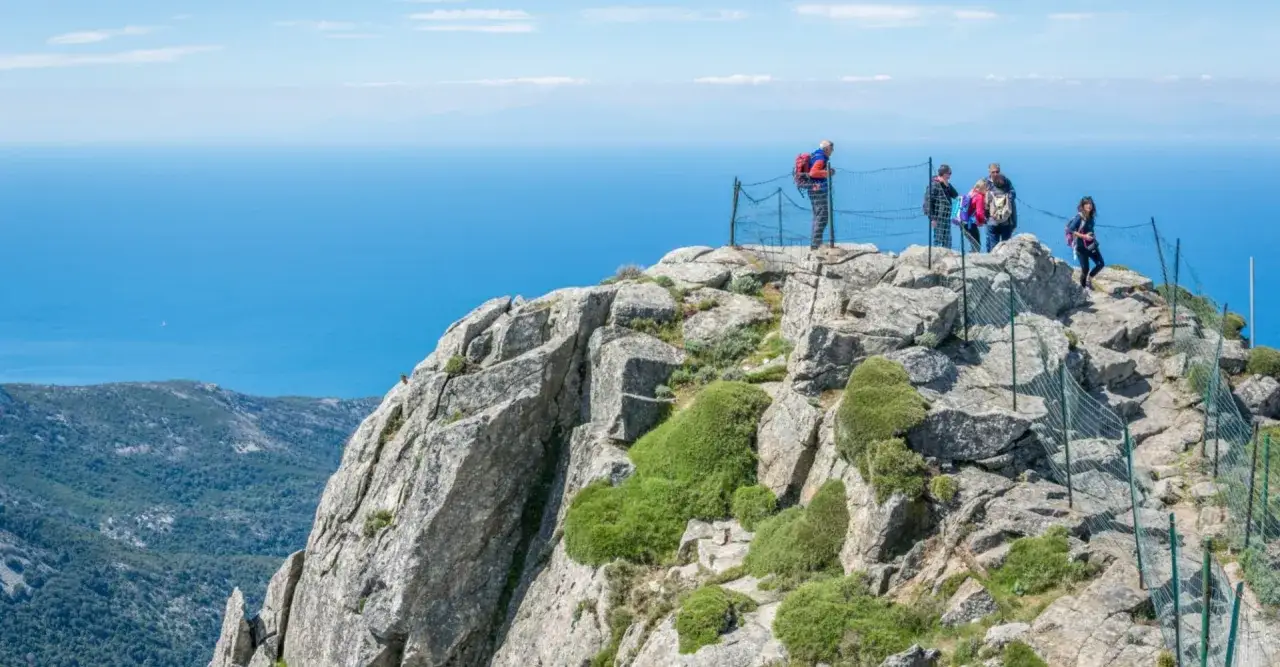 Escursionisti ammirano il panorama dal crinale roccioso, un'esperienza di trekking toscana montagna con vista sul mare blu.