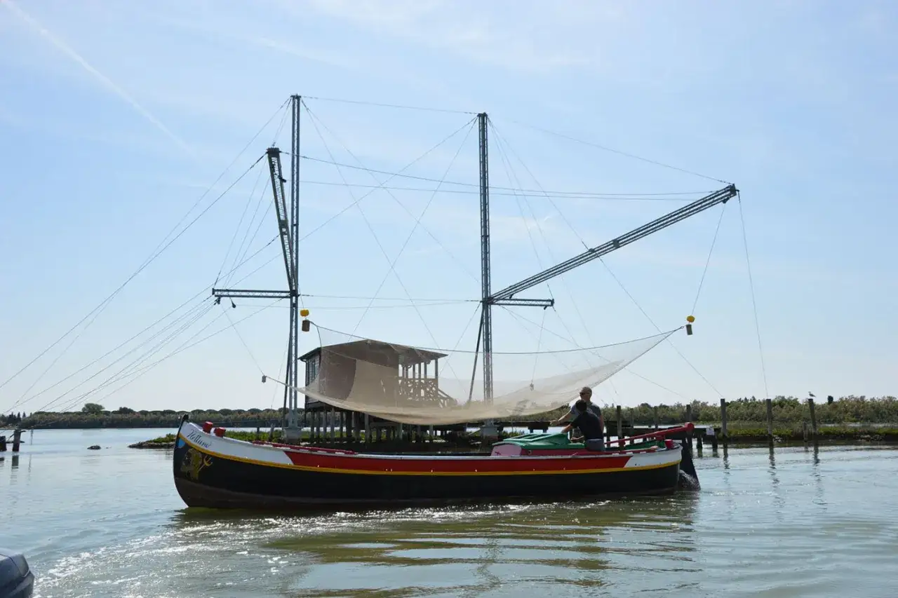 Barca da pesca con reti e capanna su palafitte, un'esperienza di pesca turismo in un paesaggio lagunare.