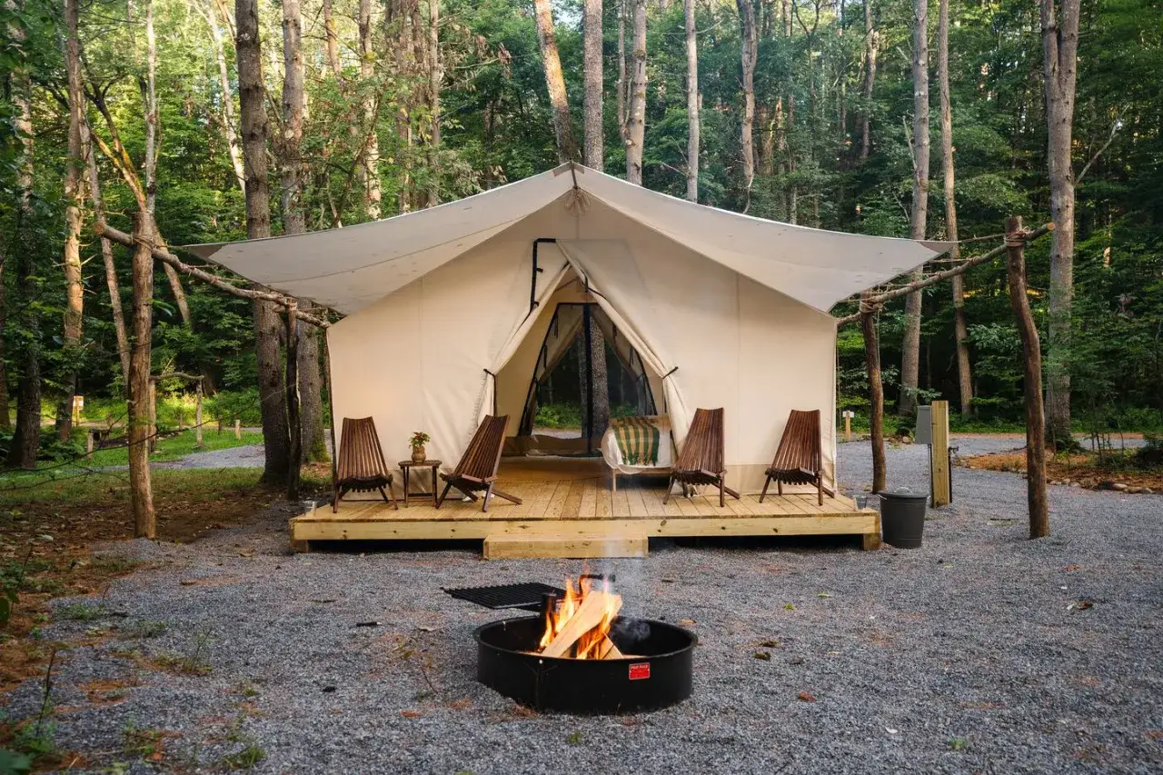 Tenda da glamping immersa nel bosco, con un falò acceso e sedie in legno. Perfetto per un'avventura di glamping bambini indimenticabile.