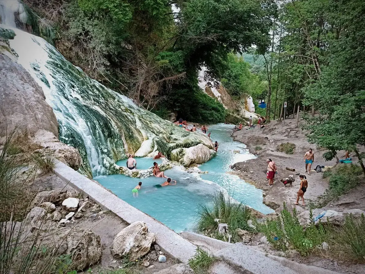 Cascate naturali con acqua turchese e persone che si rilassano, un'oasi di pace a Borgo San Filippo.