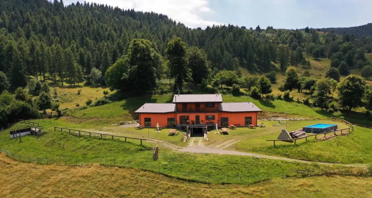 Agriturismi Lombardia montagna: casa arancione con piscina, immersa nel verde di un bosco lussureggiante.