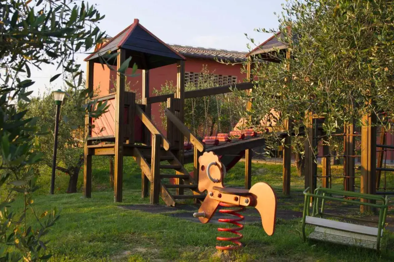Un parco giochi in Toscana, tra ulivi, pronto per i bambini. Altalena, cavalluccio a molla e struttura in legno invitano al gioco.