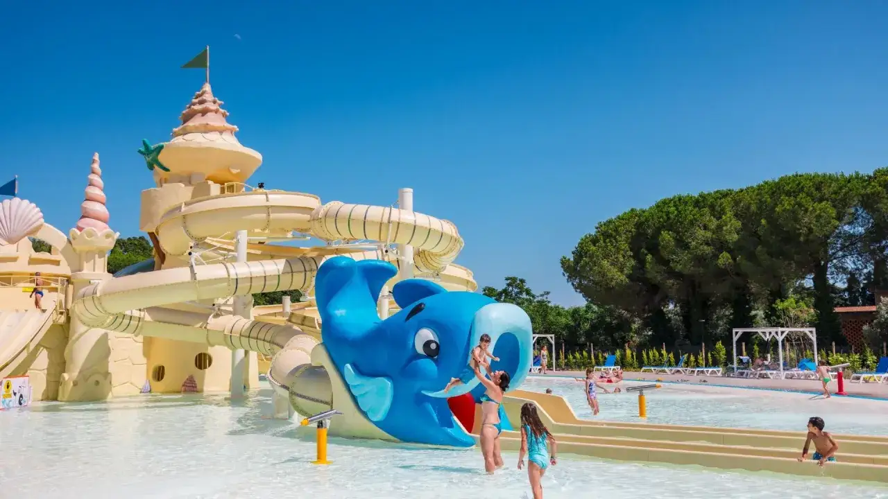 Un villaggio famiglie in Toscana con scivoli acquatici a forma di balena e castello. Bambini giocano felici nell'acqua cristallina.