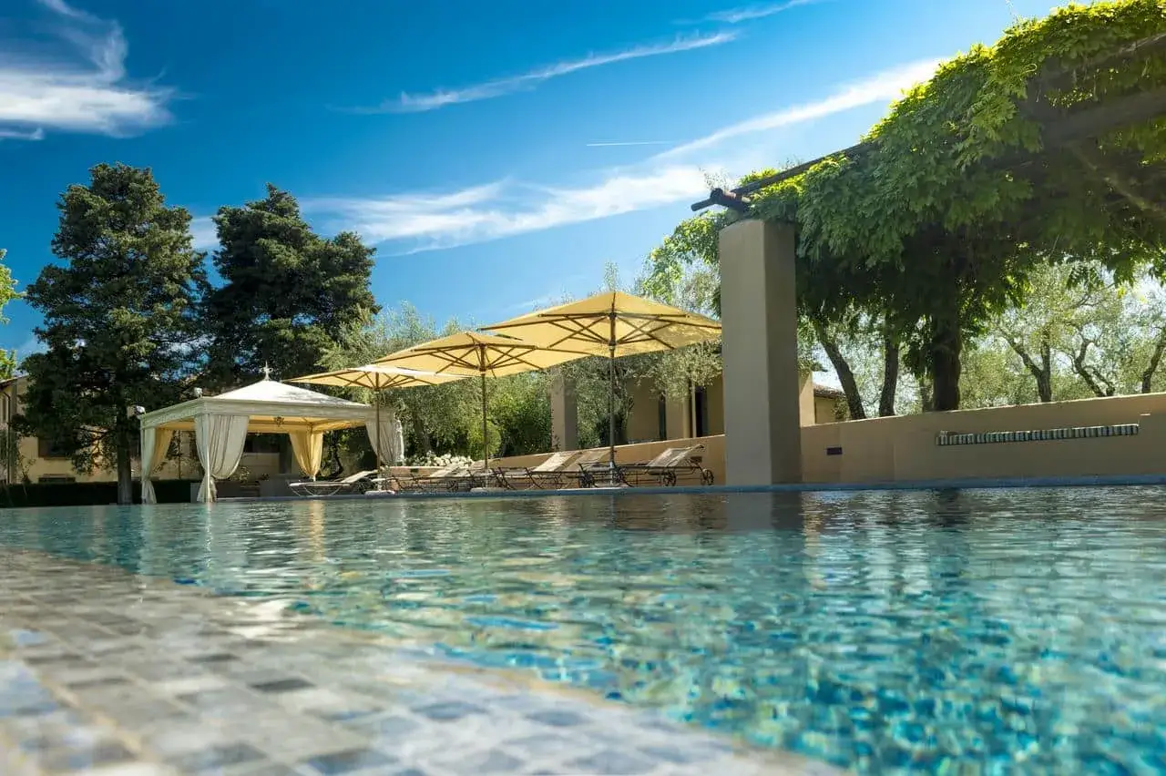 Piscina scintillante con lettini e ombrelloni, un gazebo bianco e alberi verdi, tipico di agriturismi centro Italia.