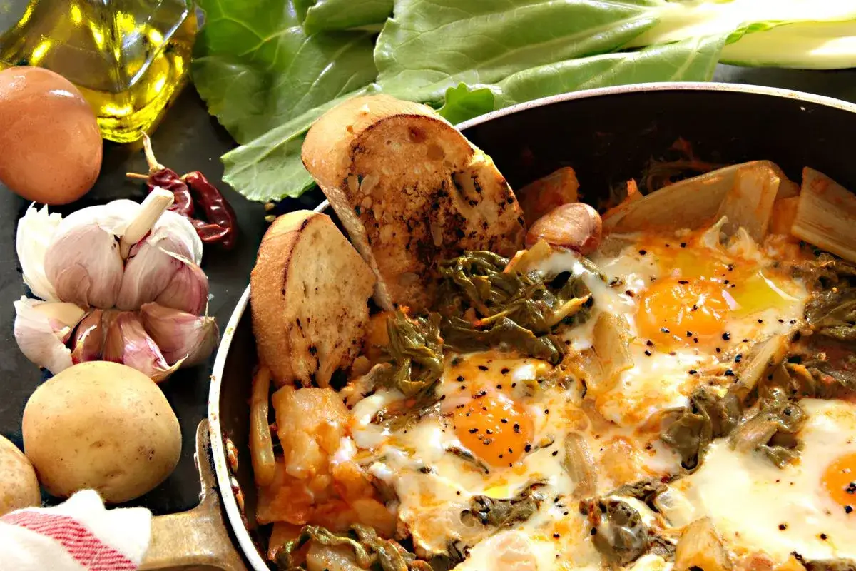 Uova cotte in padella con verdure, patate, aglio, peperoncino e pane tostato. Un piatto rustico e saporito, perfetto per una colazione o un pranzo veloce.