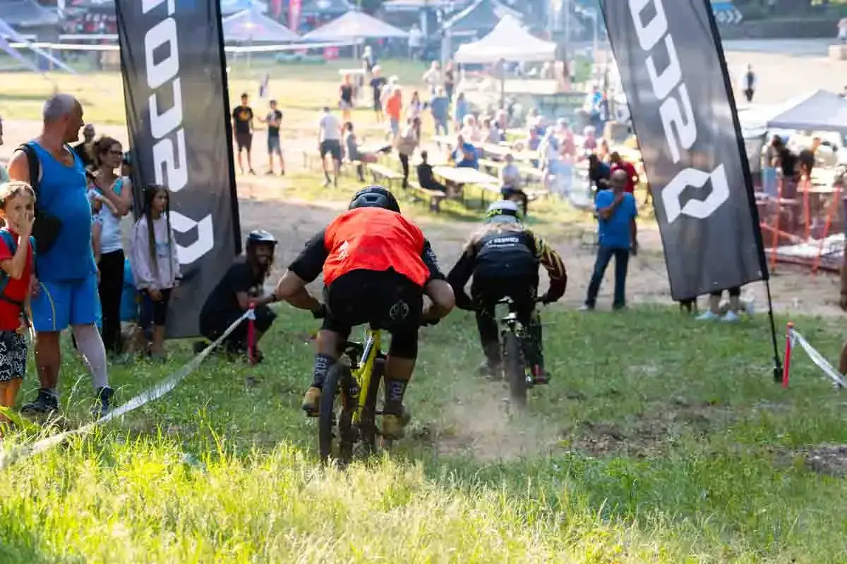 Ciclisti in gara, con bandiere che ricordano gli impianti Amiata. La folla assiste all'evento sportivo.
