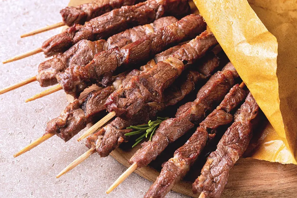 Arrosticini, uno dei piatti tipici abruzzesi, su uno spiedo di legno, pronti per essere gustati.
