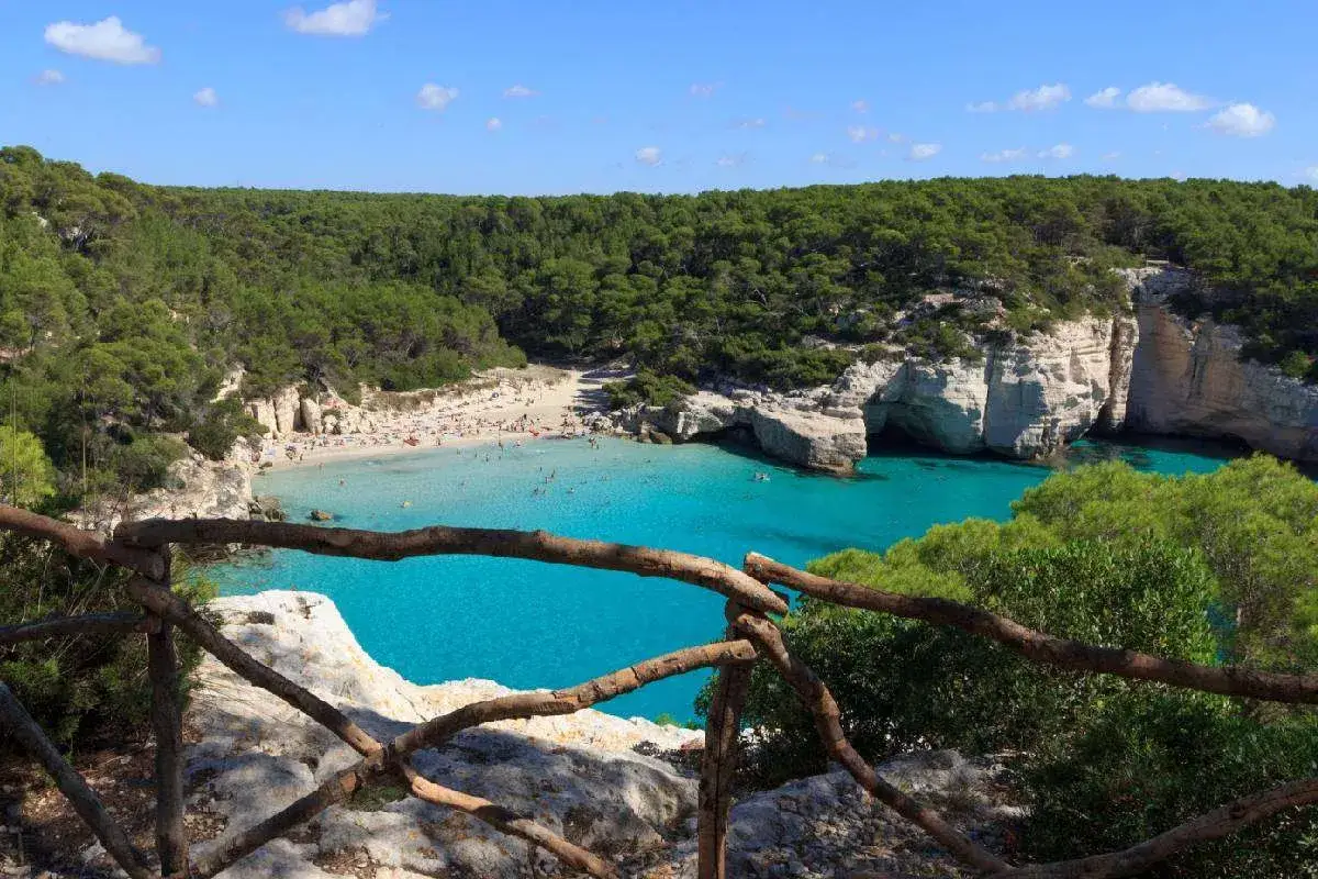 Splendida baia con acque turchesi, spiaggia affollata e scogliere verdi. Un sentiero per trekking sul mare toscana offre una vista mozzafiato.