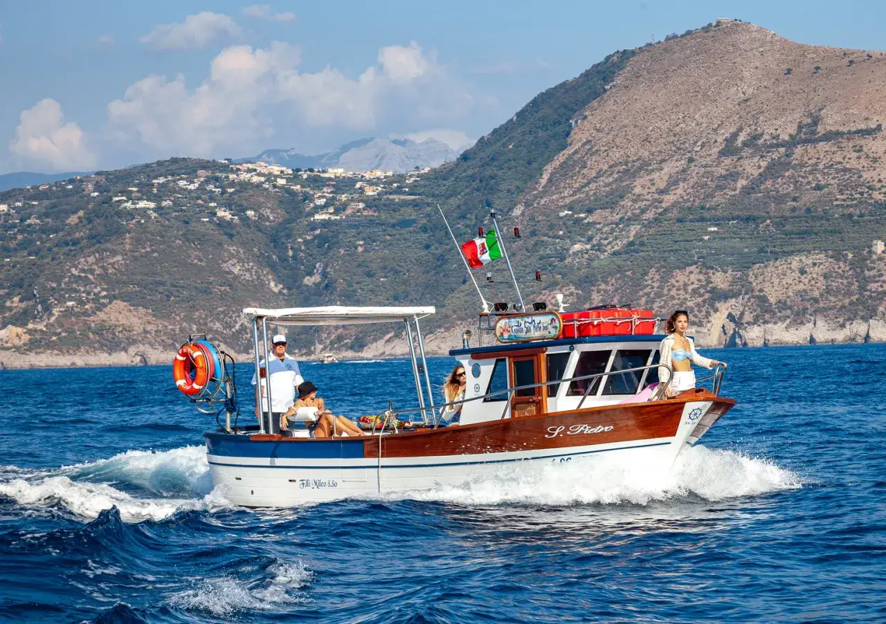 Gente a bordo di una barca per pescaturismo, con un paesaggio collinare sullo sfondo.