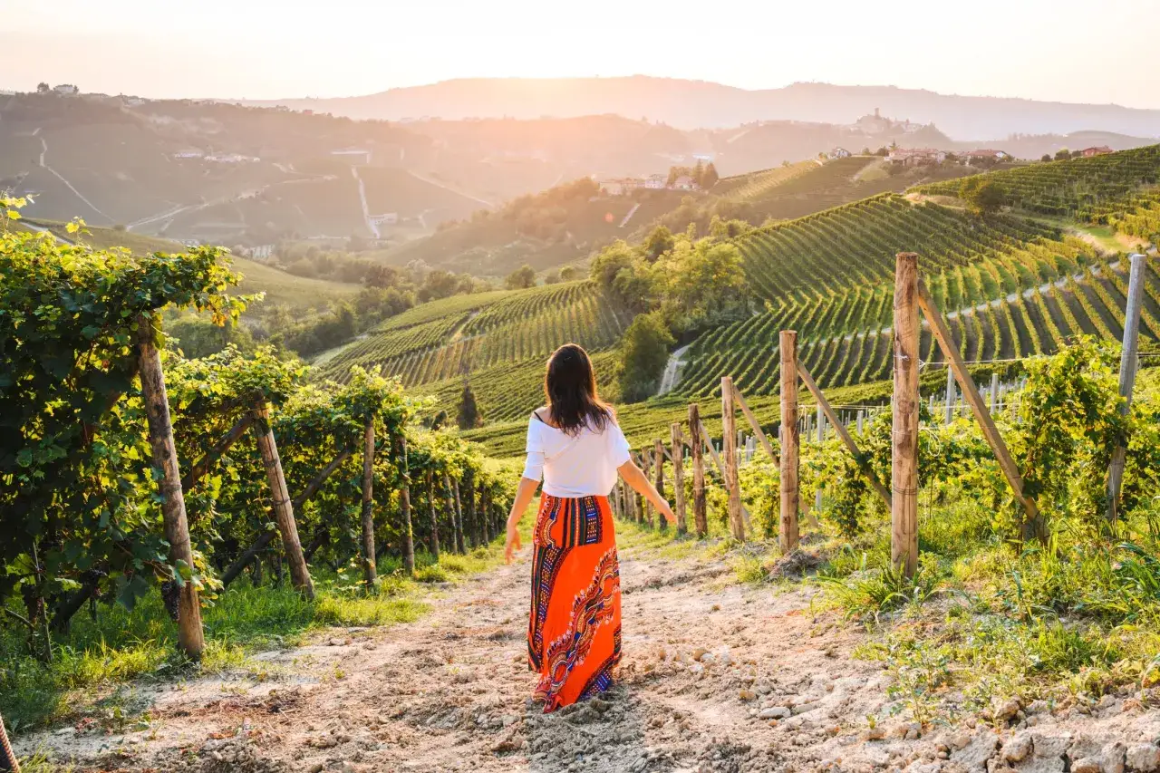 Donna in un vigneto al tramonto, perfetta per una vacanza enogastronomica tra le colline.