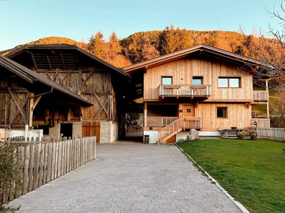 Un casolare in legno con un fienile antico. Il sole del tramonto illumina le colline dietro, creando un'atmosfera calda, come quella di un gallo rosso masi che canta all'alba.