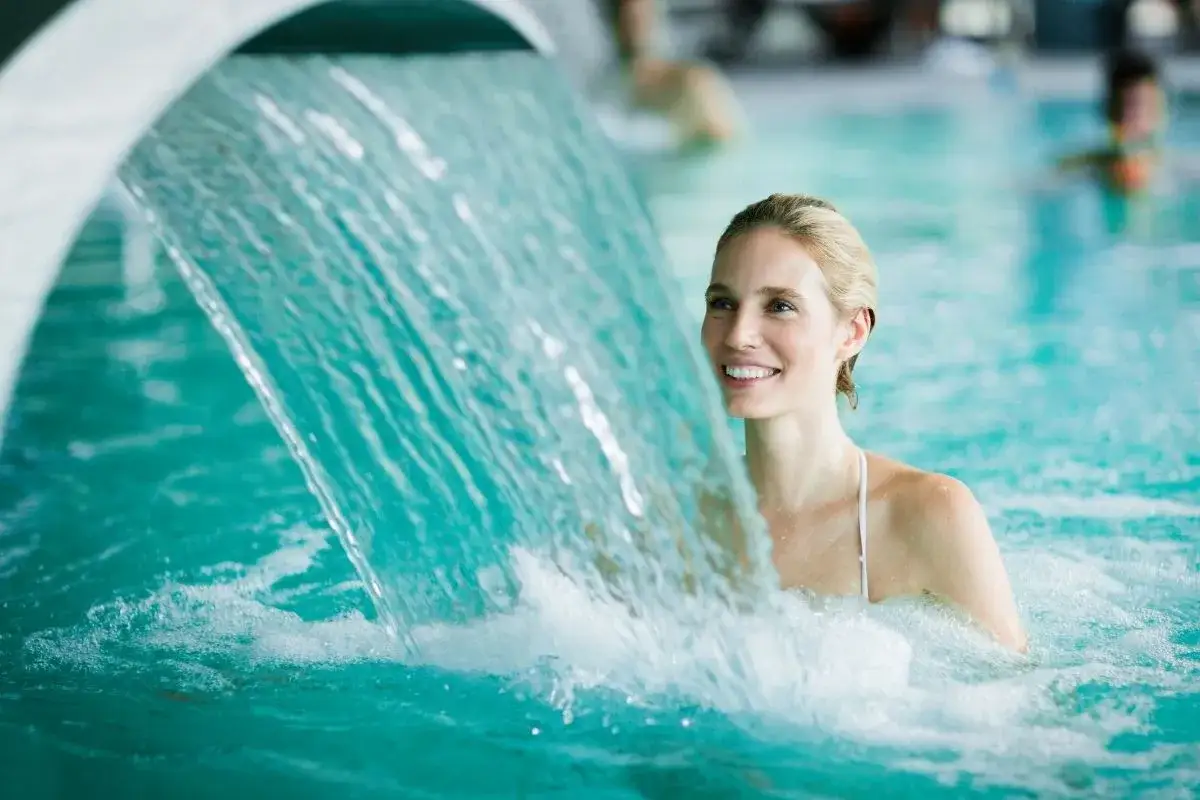 Donna sorridente sotto una cascata d'acqua in una piscina di uno spa in Piemonte. Relax e benessere.