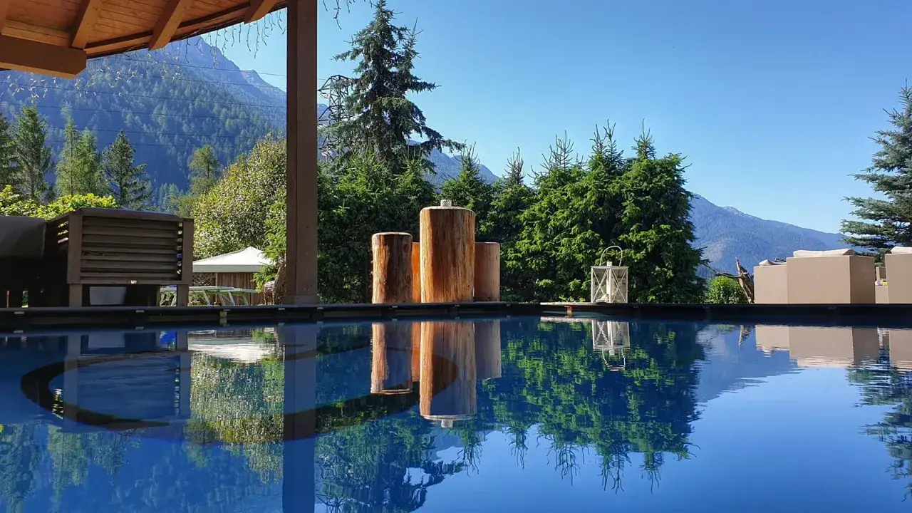 Rilassante piscina in montagna Piemonte, con riflessi sull'acqua e vista su boschi e cime.