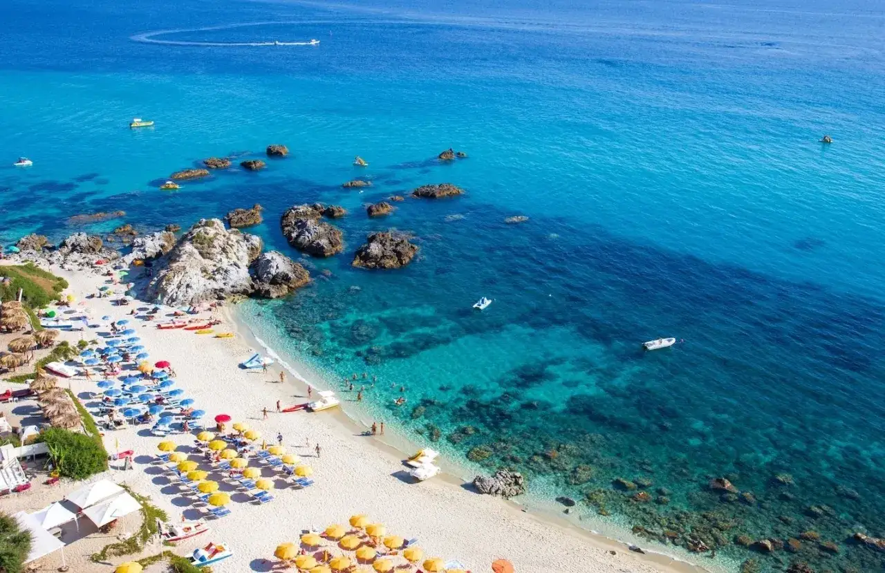 Spiaggia affollata con ombrelloni colorati e mare cristallino, ideale tra i posti da visitare in Calabria con bambini per una vacanza indimenticabile.