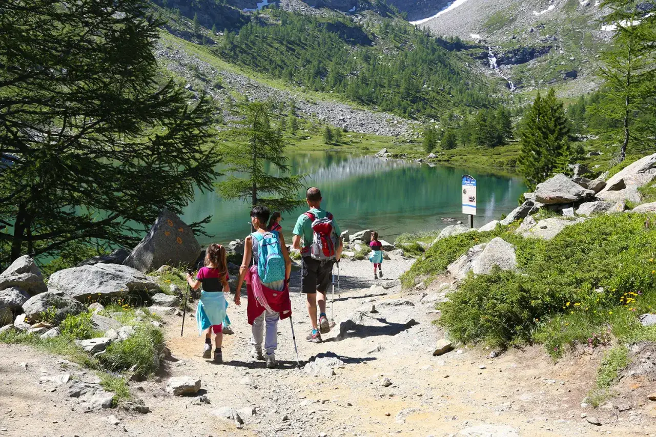 Famiglia in escursione nella valle d'Aosta con bambini in estate, verso un lago alpino turchese.
