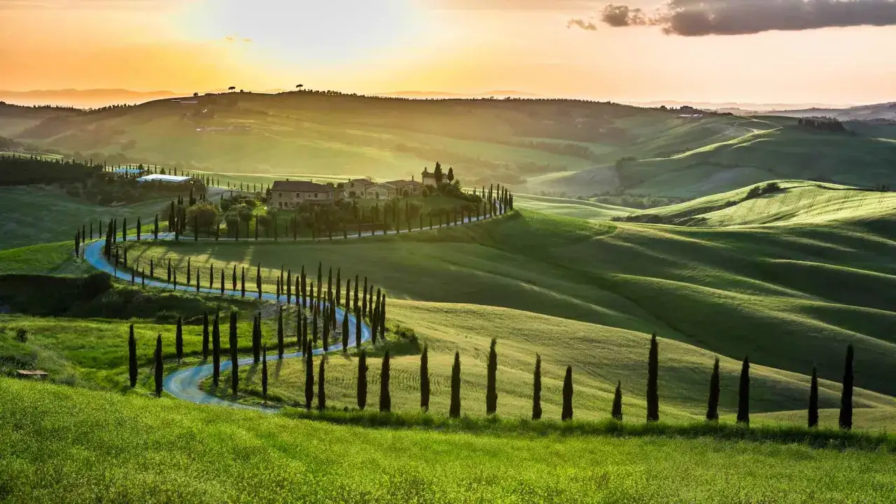 Strade panoramiche toscana serpeggiano tra dolci colline verdi, fiancheggiate da cipressi e illuminate dal sole al tramonto.