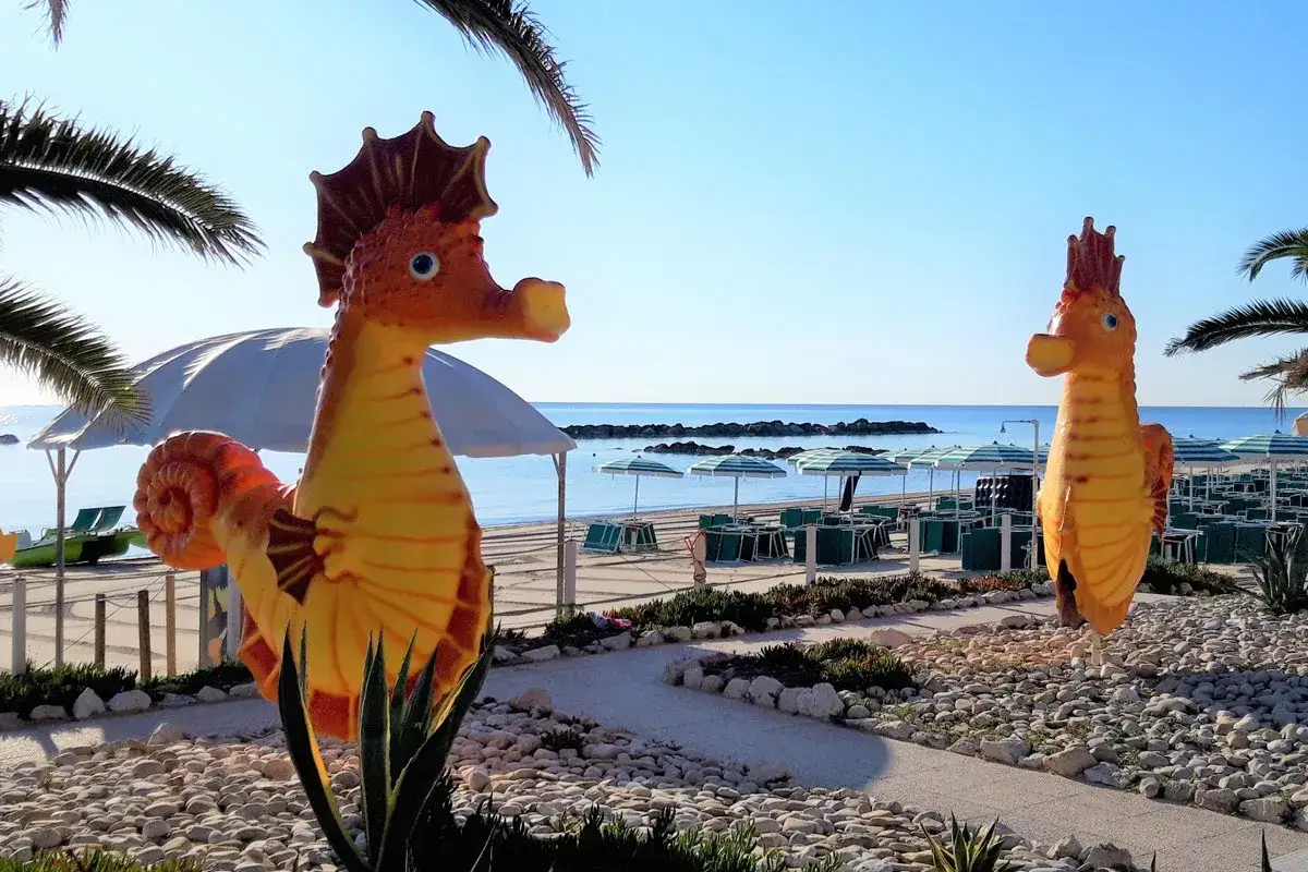 Due cavallucci marini decorativi accolgono i visitatori al camping Riva Verde Marche, con il mare azzurro e ombrelloni pronti per l'estate.
