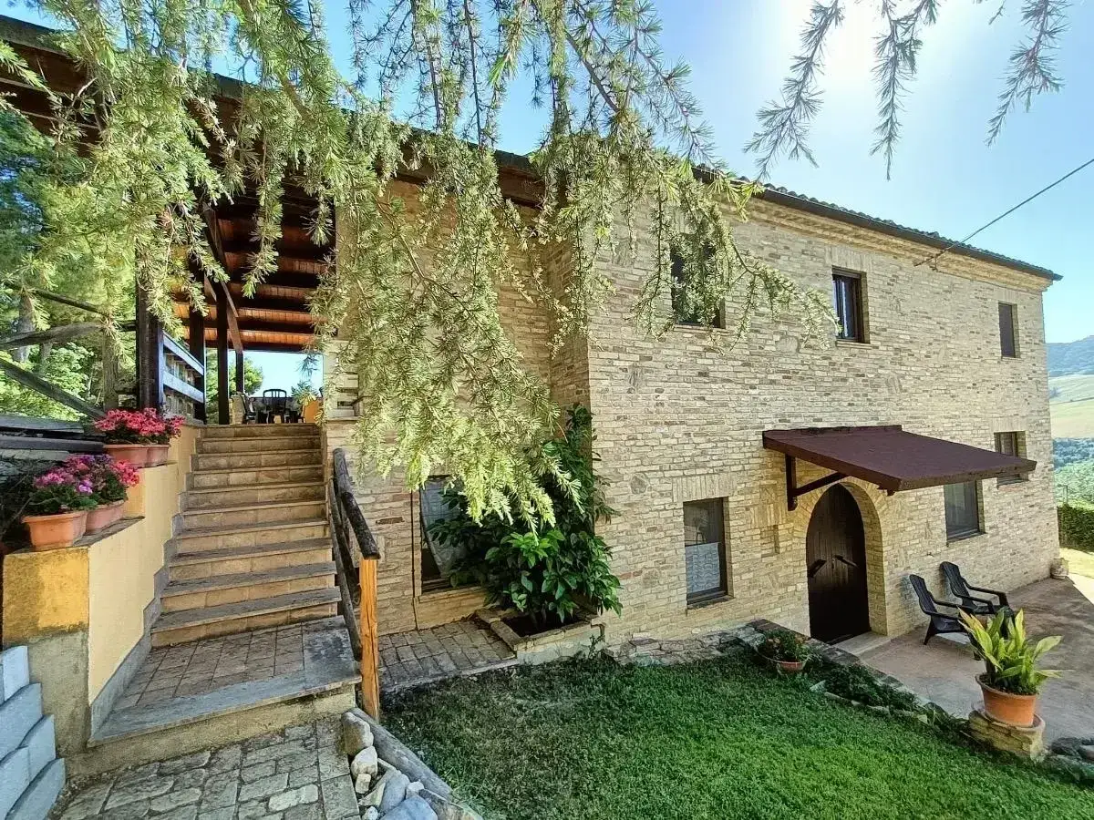 Casa in pietra con scale e fiori, immersa nel verde dell'entroterra marchigiano. Un luogo sereno per godersi la natura.