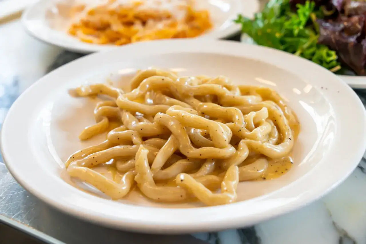 Pici cacio e pepe, uno dei piatti tipici di Siena, serviti su un piatto bianco.