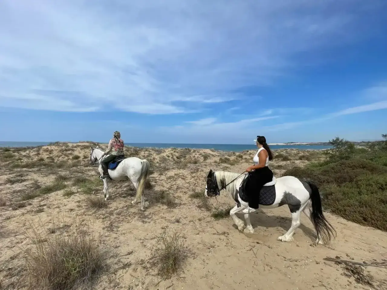 Due donne fanno una passeggiata a cavallo in Sicilia, su un sentiero sabbioso vicino al mare.