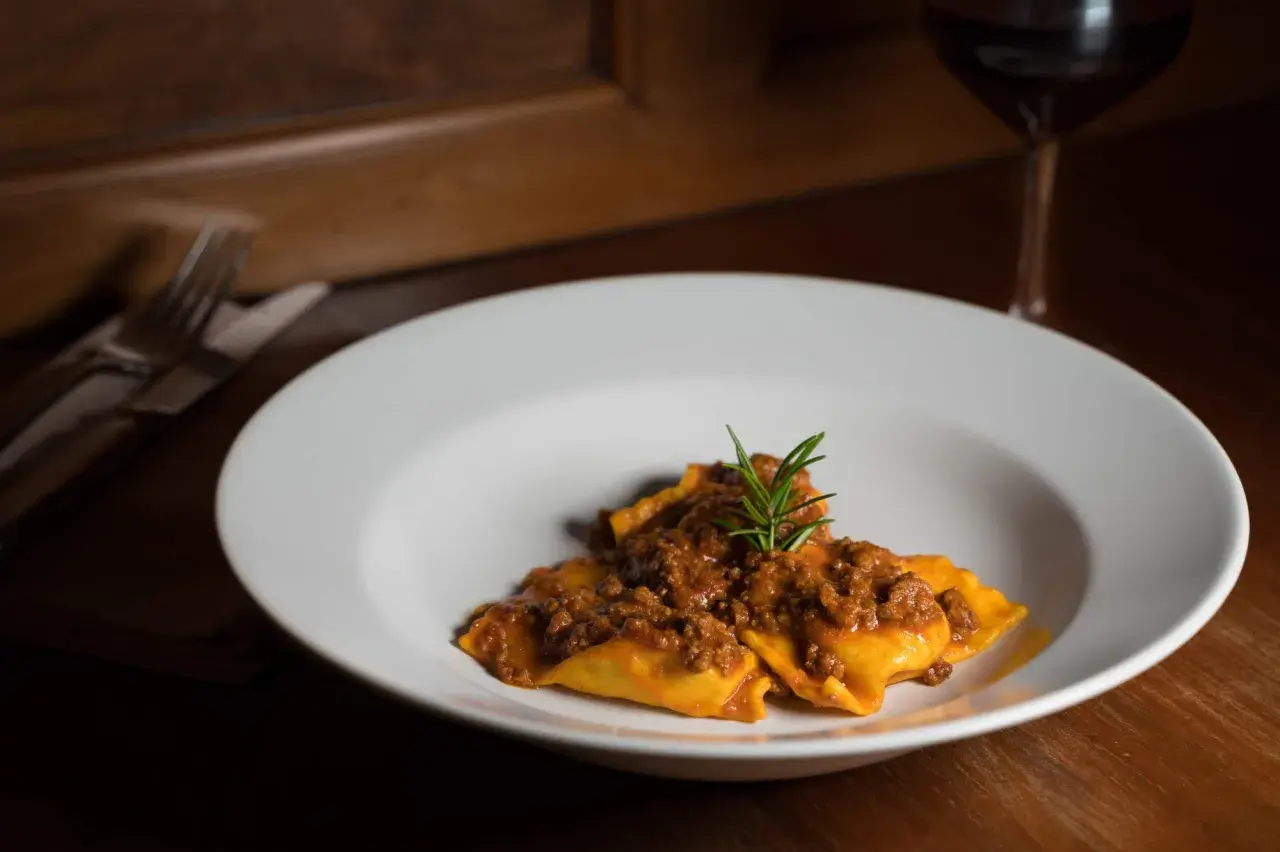 Tortelli di patate del Mugello, un piatto ricco e saporito, servito su un piatto bianco con un rametto di rosmarino.