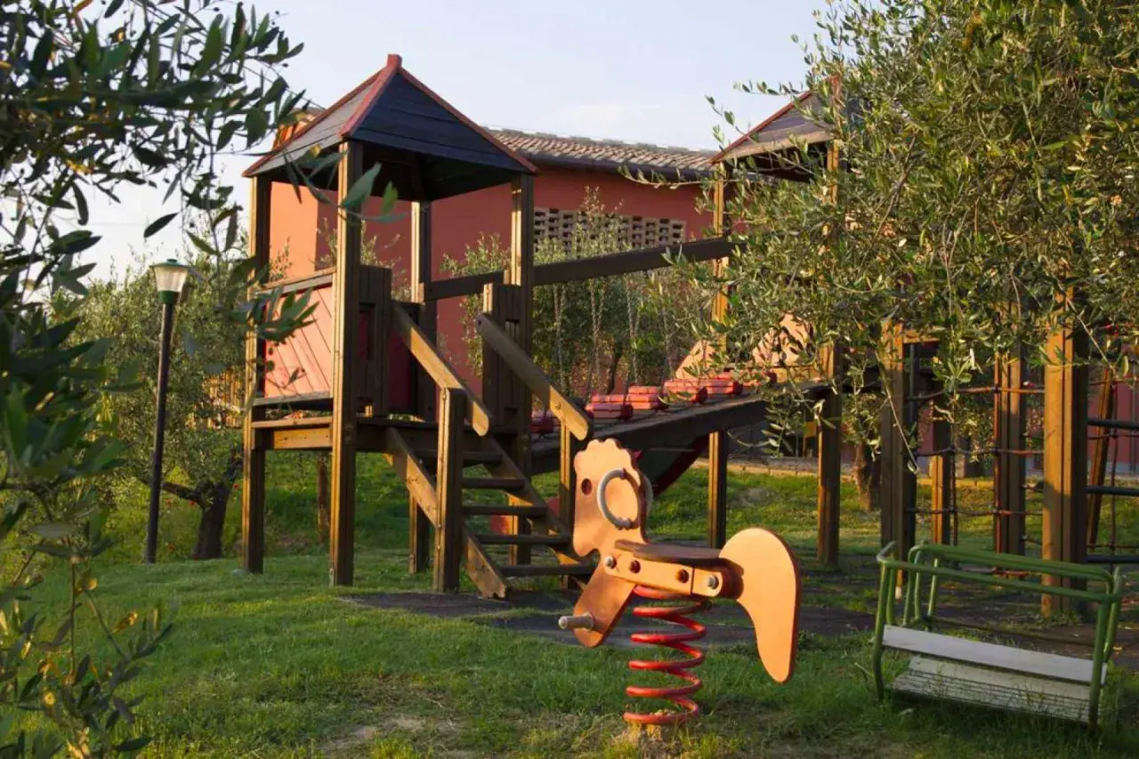 Un parco giochi in Toscana, tra ulivi, pronto per i bambini. Altalena, cavalluccio a molla e struttura in legno invitano al gioco.