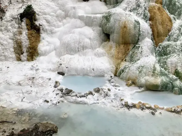 Cascate bianche e rocce calcaree ai Bagni San Filippo, con piccole pozze d'acqua azzurra che riflettono il paesaggio surreale.