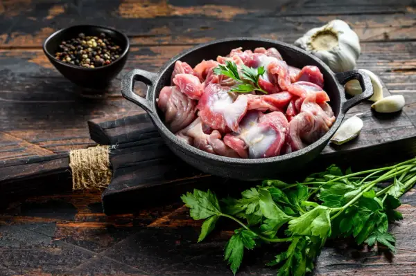 Piatto toscano con interiora di pollo crude in padella, con aglio, pepe e prezzemolo su tagliere di legno scuro.